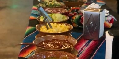 A table with bowls of salsa and accompaniments on a colorful cloth.