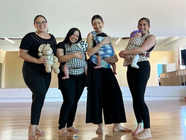 Four women standing barefoot, each holding a baby or teddy bear.