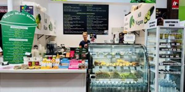 A cozy cafe counter with a smiling barista and a variety of food and drinks on display.