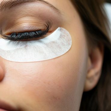 Close-up of a woman's eye with a white under-eye patch and long eyelashes.