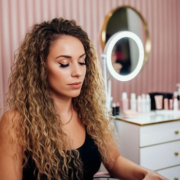 Woman with curly hair sitting in a beauty studio with makeup products.
