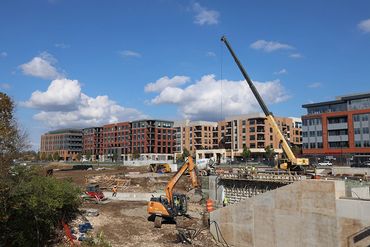 Construction site with equipment and workers near modern apartment buildings under a blue sky.