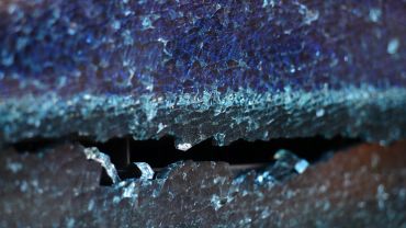 Close-up of shattered blue tempered glass with a jagged opening.