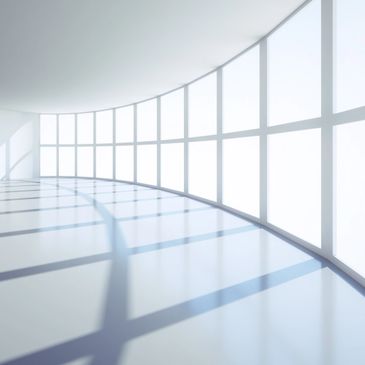 Bright curved corridor with large grid windows casting shadows on the floor.