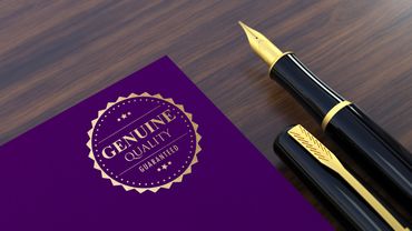 A black and gold fountain pen next to a purple card with a gold 'Genuine Quality Guaranteed' seal.