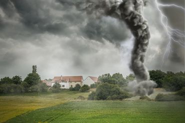 A tornado with dark smoke near houses under stormy skies with lightning.