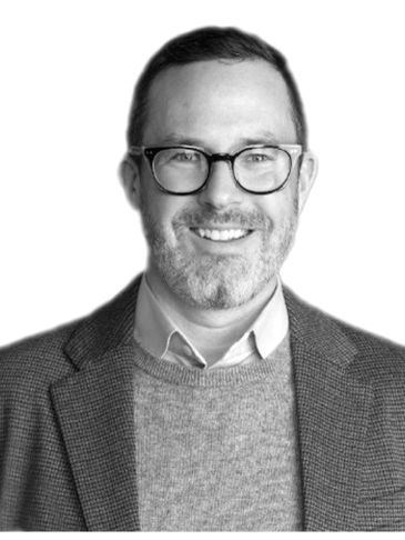 Smiling man with glasses in a sweater and blazer.