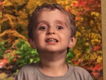 Vogm boy in school picture, smiling with fall leaves background.