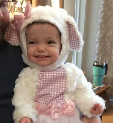 Vogm baby girl smiling 
 in white and pink lamb costume.