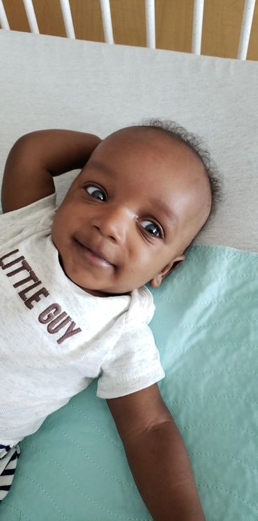 Vein of galen Malformation (VOGM/VGM) baby boy smiling, wearing a “little guy” shirt.