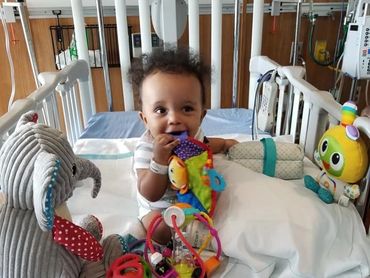 Little vogm boy sitting up in hospital bed surrounded by toys after his embolization.