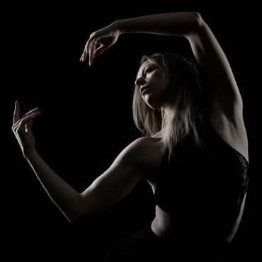 Graceful dancer posing with elegant arm movements against a black background.