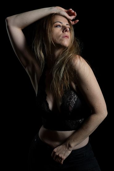 Woman posing in black lace top against a dark background.