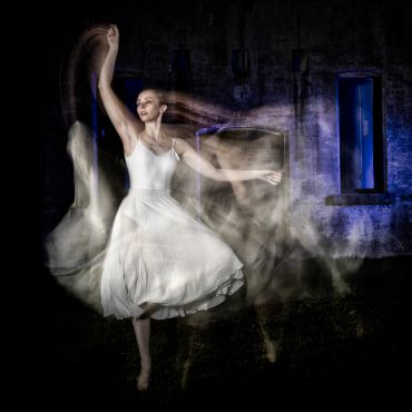 Ballerina dancing gracefully with motion blur in a dimly lit setting.