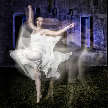 A dancer in white dress captured with motion blur against a dark background.