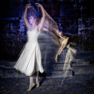 A ballerina in a white dress captured in a graceful motion blur against a dark background.