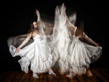 A dancer in a flowing white dress captured in motion against a black background.