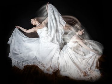Dancer in a flowing white dress captured in motion against a dark background.