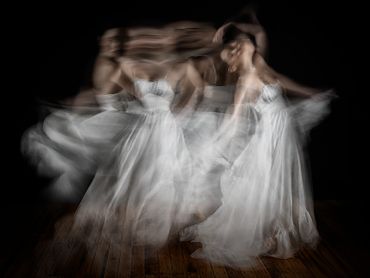Blurred motion of a woman dancing gracefully in a flowing white dress.