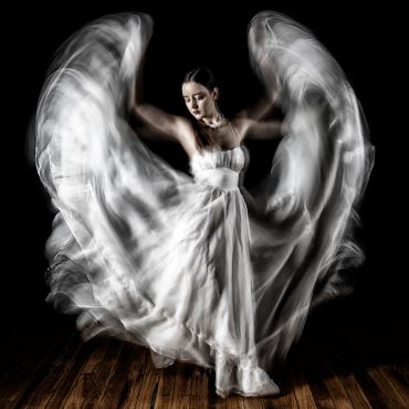 A dancer in a flowing white dress creates wing-like motion with her arms.