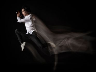 Man in white shirt and black pants leaps dynamically against a dark background.