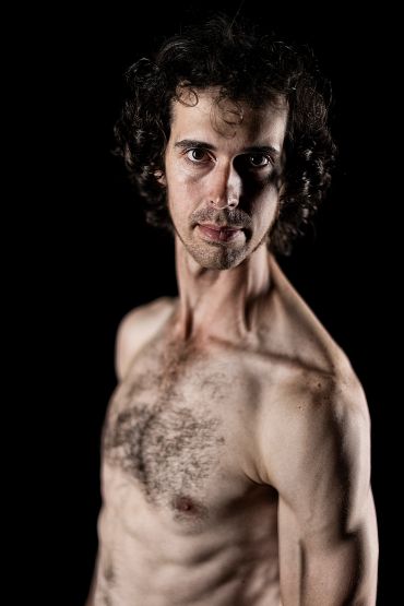 Portrait of a shirtless man with curly hair against a dark background.