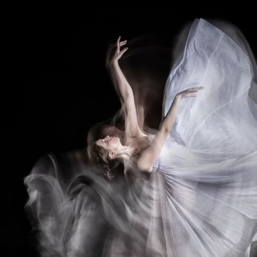A graceful dancer in a flowing white dress captured with motion blur against a black background.
