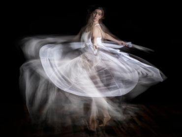 A dancer twirling in a flowing white dress with motion blur.