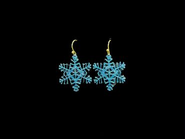 Blue snowflake-shaped earrings with gold hooks on black background.