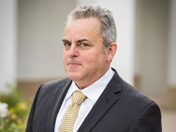Man in a black pinstripe suit with a yellow tie posing outdoors.