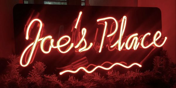Neon sign reading 'Joe's Place' in glowing red light.