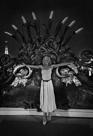 A woman posing joyfully with arms outstretched in front of ornate backdrop.