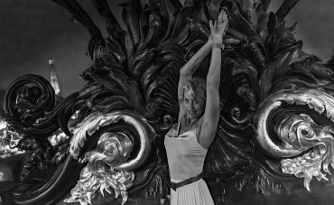 Woman posing with arms raised against an ornate background.