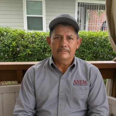 Man sitting on a porch wearing a gray ANEM shirt and cap.