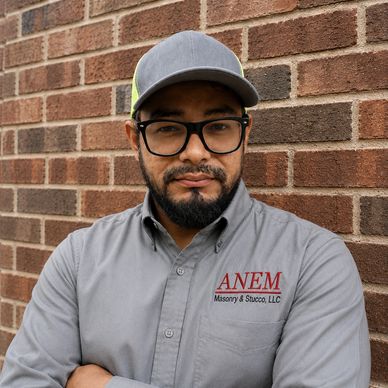 Man wearing company shirt posing against brick wall.