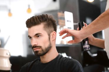 A man getting his hair styled with hair spray in a modern salon.