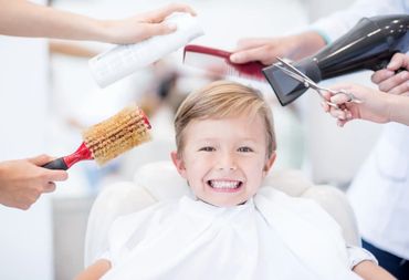 Smiling boy surrounded by hair styling tools at a salon.