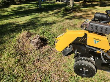 A yellow Vermeer stump grinder next to a tree stump on grass.