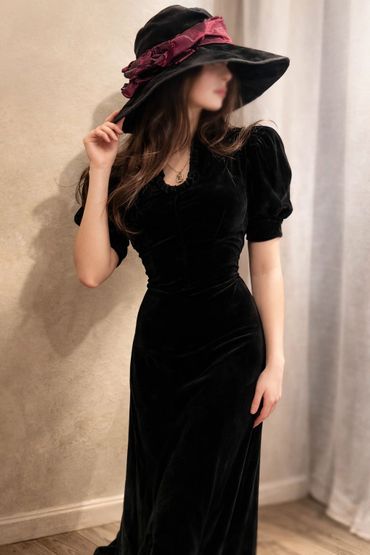 Woman in elegant black velvet dress and wide-brimmed hat with a red ribbon.