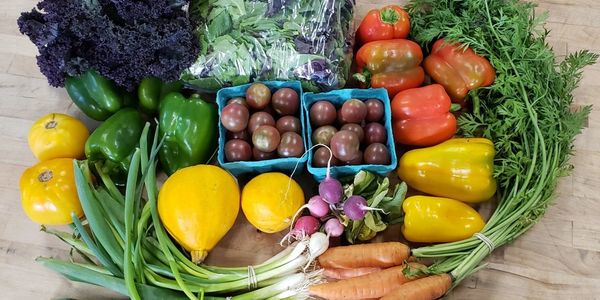 A bundle of colorful vegetables laid out on a wood table: Carrots, tomatoes, bell peppers, greens.
