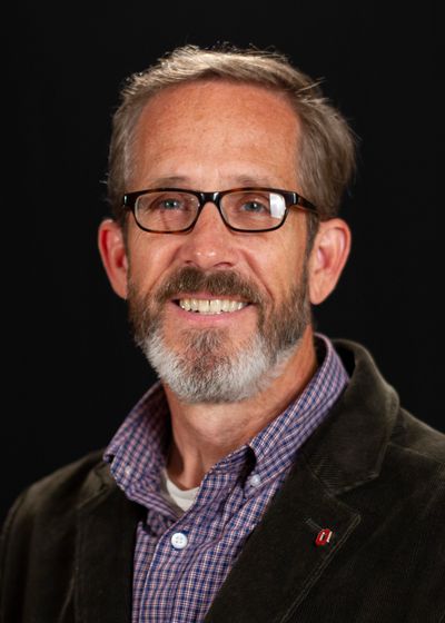 CLose-up of Kip Curtis, a light-skinned man, wears black rimmed glasses, a checkered patterned shirt
