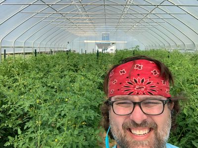 A selfie of Tim Hicks, a light skinned man, wearing a red bandana in front of a green growing crop!