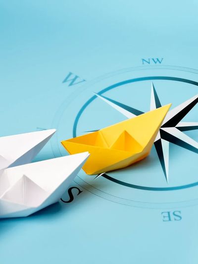 Un bateau en papier jaune mène une flotte de bateaux blancs sur un fond représentant une boussole.