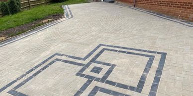 Newly paved driveway with decorative black square patterns near a brick house.