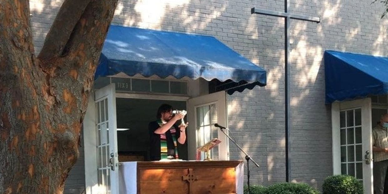 Priest celebrating the sacrament of Eucharist outside over a small wooden table.
