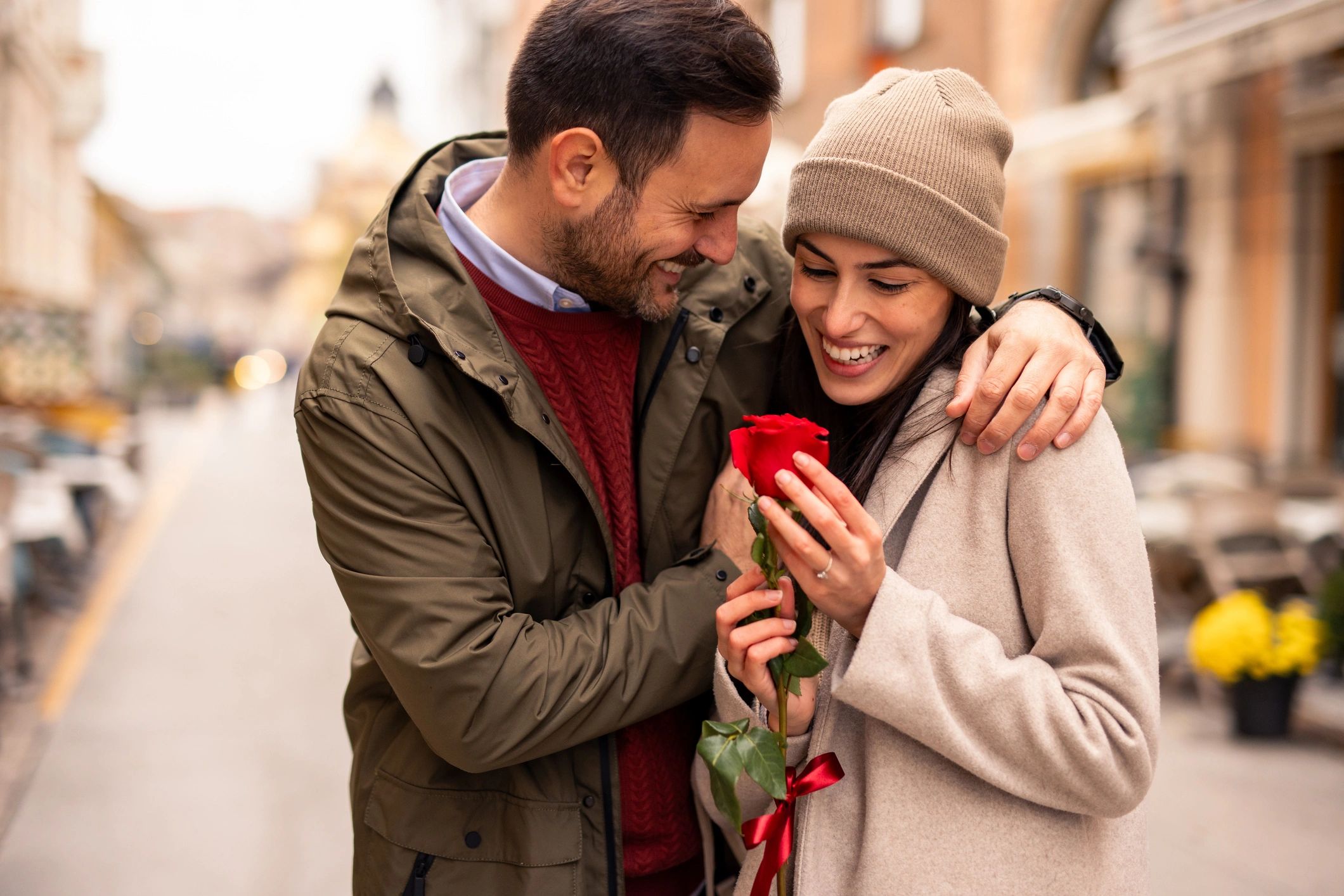 Man giving a red rose to a smiling woman on a city street. Valentine's Day.
