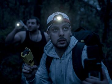 Two men with headlamps exploring a dark forest at night.