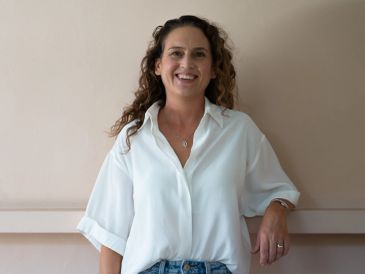 Smiling woman with curly hair in a white blouse and jeans.