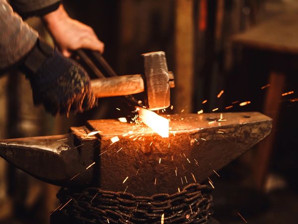The blacksmith manually forges the red-hot metal on the anvil in the forge with fireworks