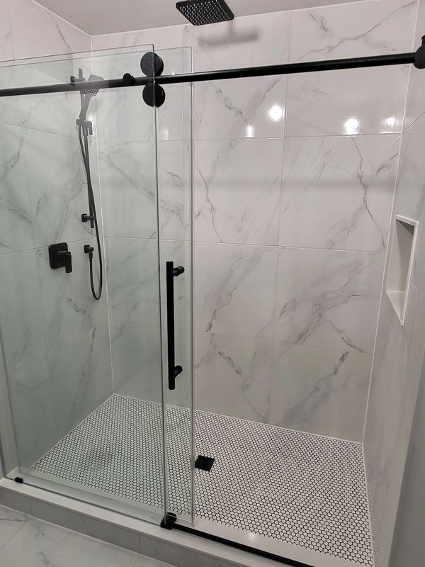 Modern shower with glass door and black fixtures in a marble-tiled bathroom.